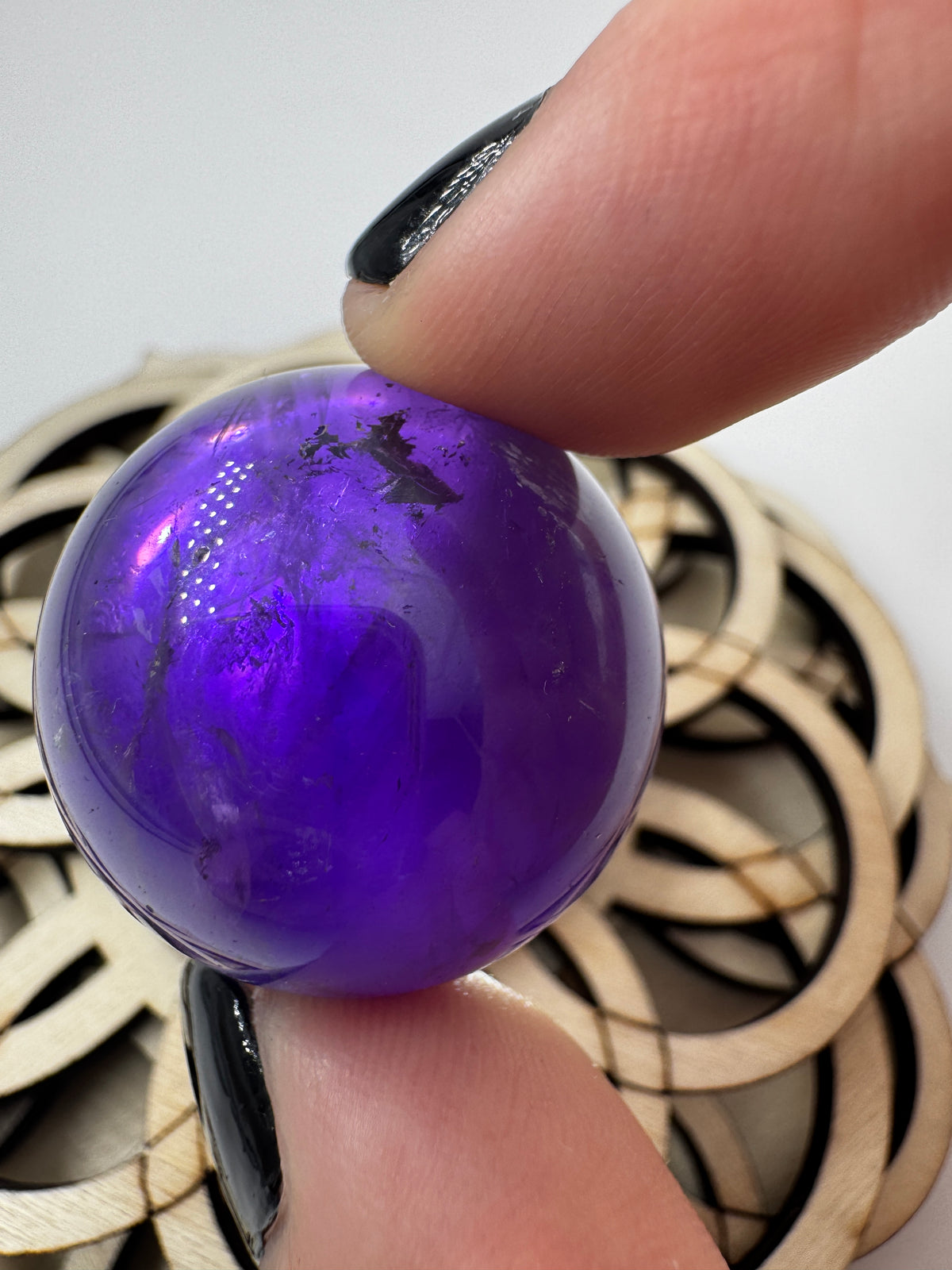 Eine hochglanzpolierte Amethyst-Kugel mit tiefvioletten Farbzentren und natürlichen Wachstumsstrukturen mit leichter Beleuchtung von hinten.