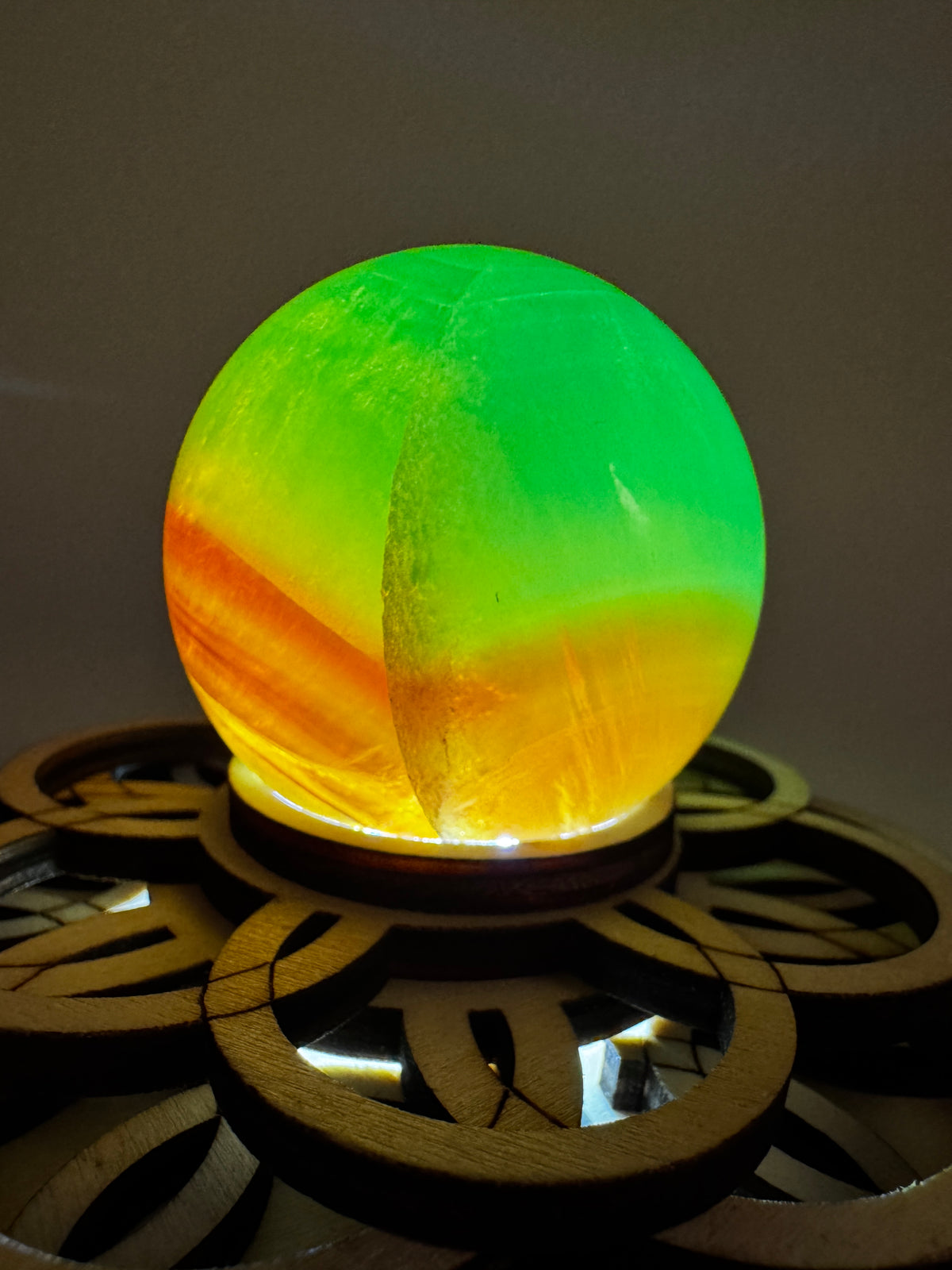 Eine Fluorit-Kugel in Grün und Orange auf einem Leuchtsockel.