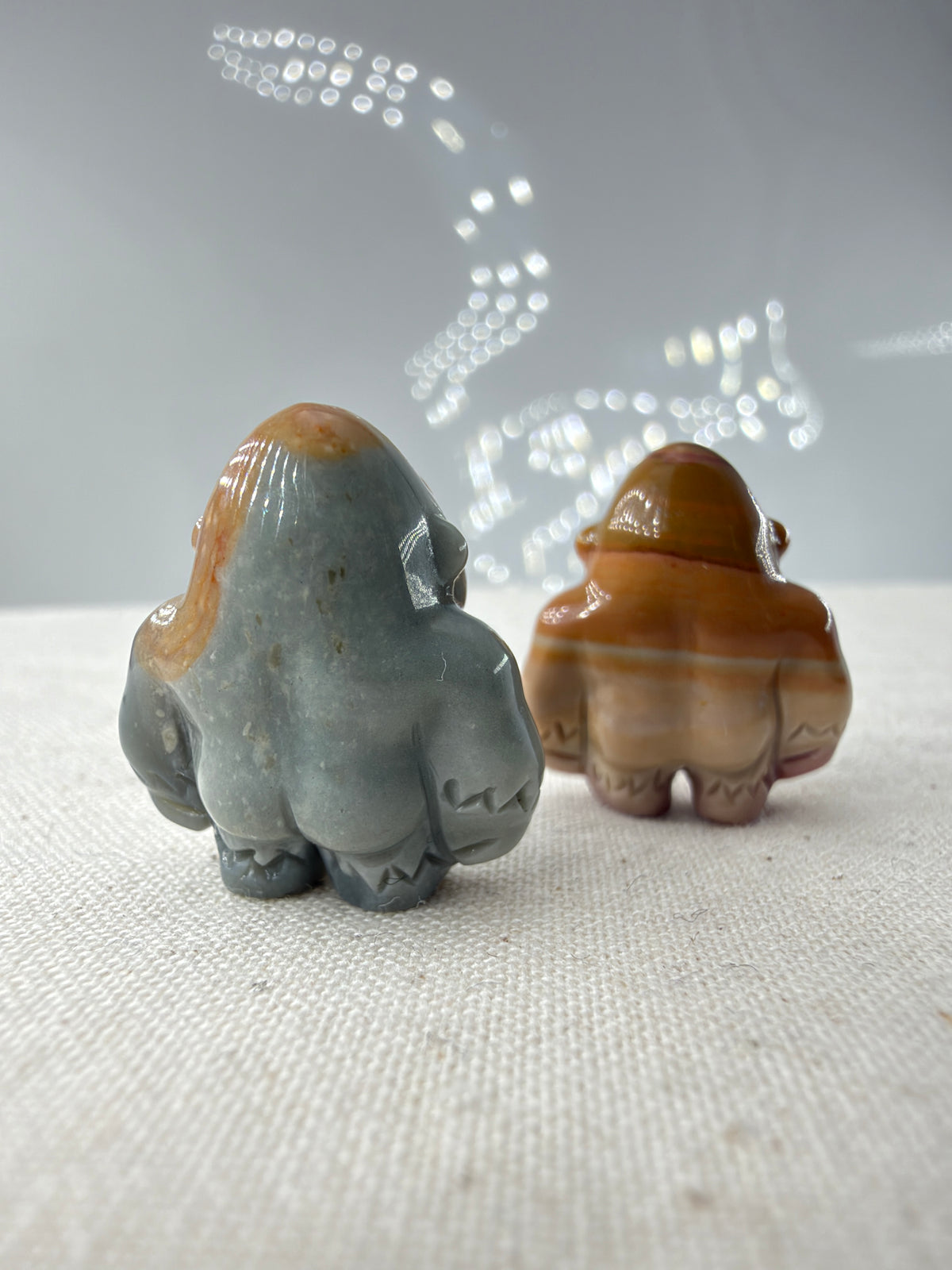 polierte Gorilla-Figuren aus Alashan-Achat, eine in Graublau und Beige, die andere in Braun und Creme, auf hellem Untergrund