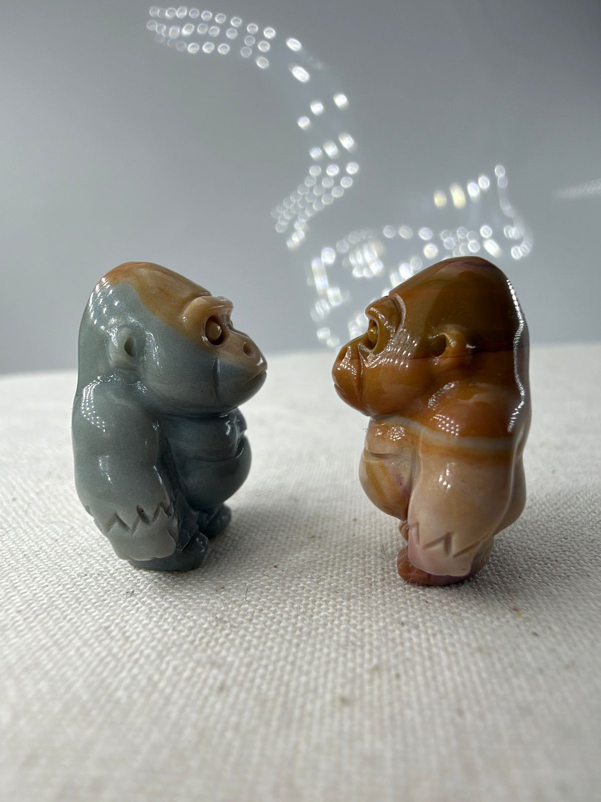 polierte Gorilla-Figuren aus Alashan-Achat, eine in Graublau und Beige, die andere in Braun und Creme, auf hellem Untergrund