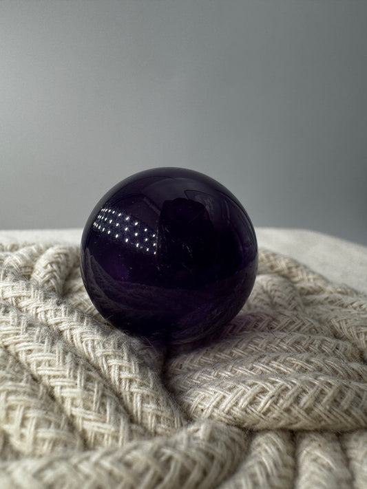 Eine hochglanzpolierte Amethyst-Kugel mit tiefvioletten Farbzentren und natürlichen Wachstumsstrukturen.