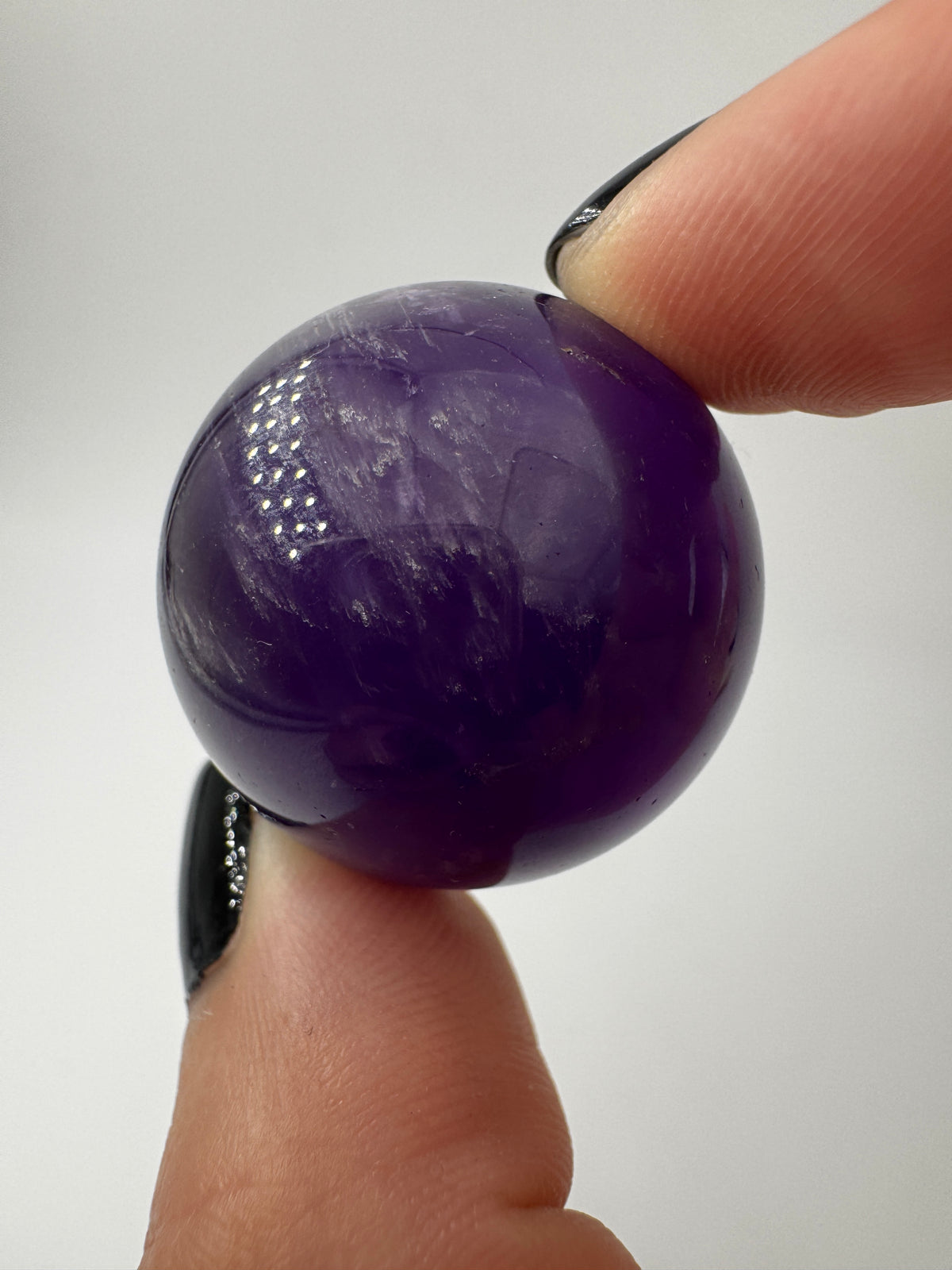Eine hochglanzpolierte Amethyst-Kugel mit tiefvioletten Farbzentren und natürlichen Wachstumsstrukturen.