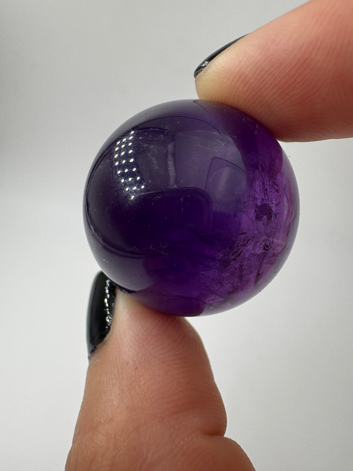 Eine hochglanzpolierte Amethyst-Kugel mit tiefvioletten Farbzentren und natürlichen Wachstumsstrukturen.