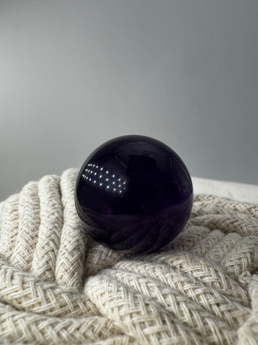 Eine hochglanzpolierte Amethyst-Kugel mit tiefvioletten Farbzentren und natürlichen Wachstumsstrukturen.