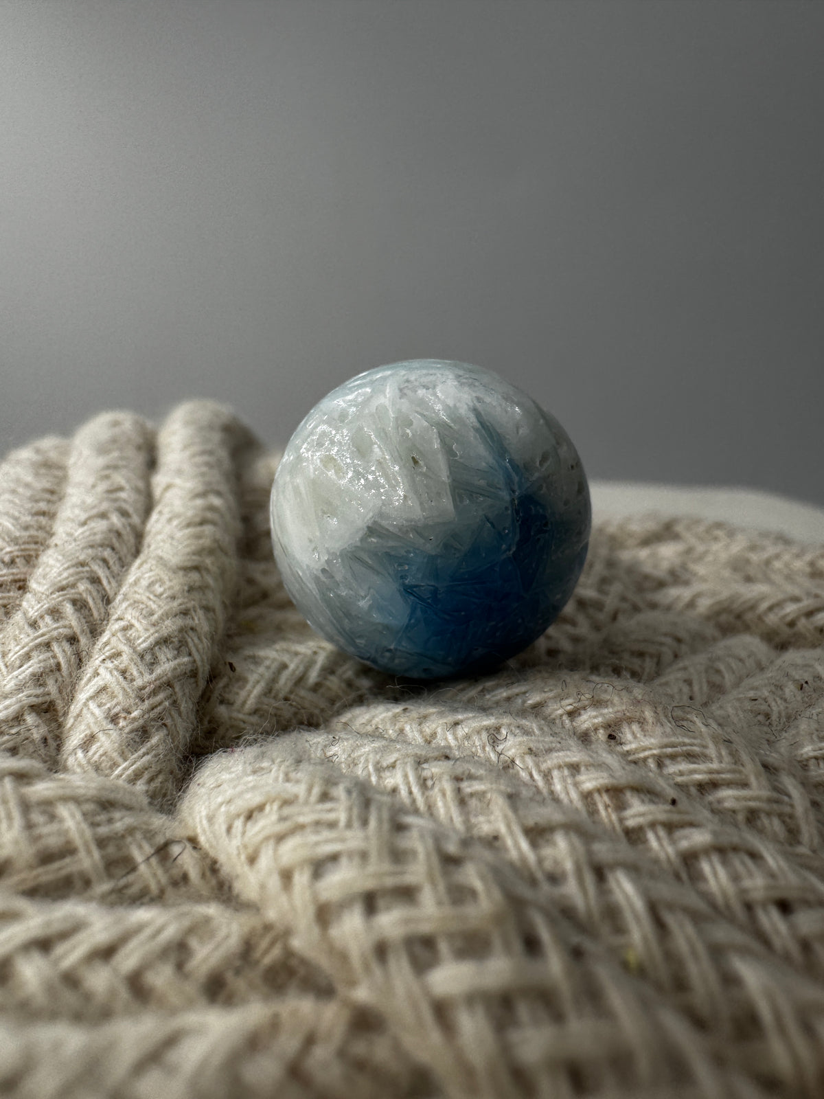 Eine perfekt sphärische Kugel aus Blue Ice Glacierite, deren glänzende Oberfläche das Licht reflektiert und den Blick auf die einmalige Strucktur freigibt.