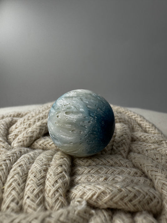 Eine perfekt sphärische Kugel aus Blue Ice Glacierite, deren glänzende Oberfläche das Licht reflektiert und den Blick auf die einmalige Strucktur freigibt.