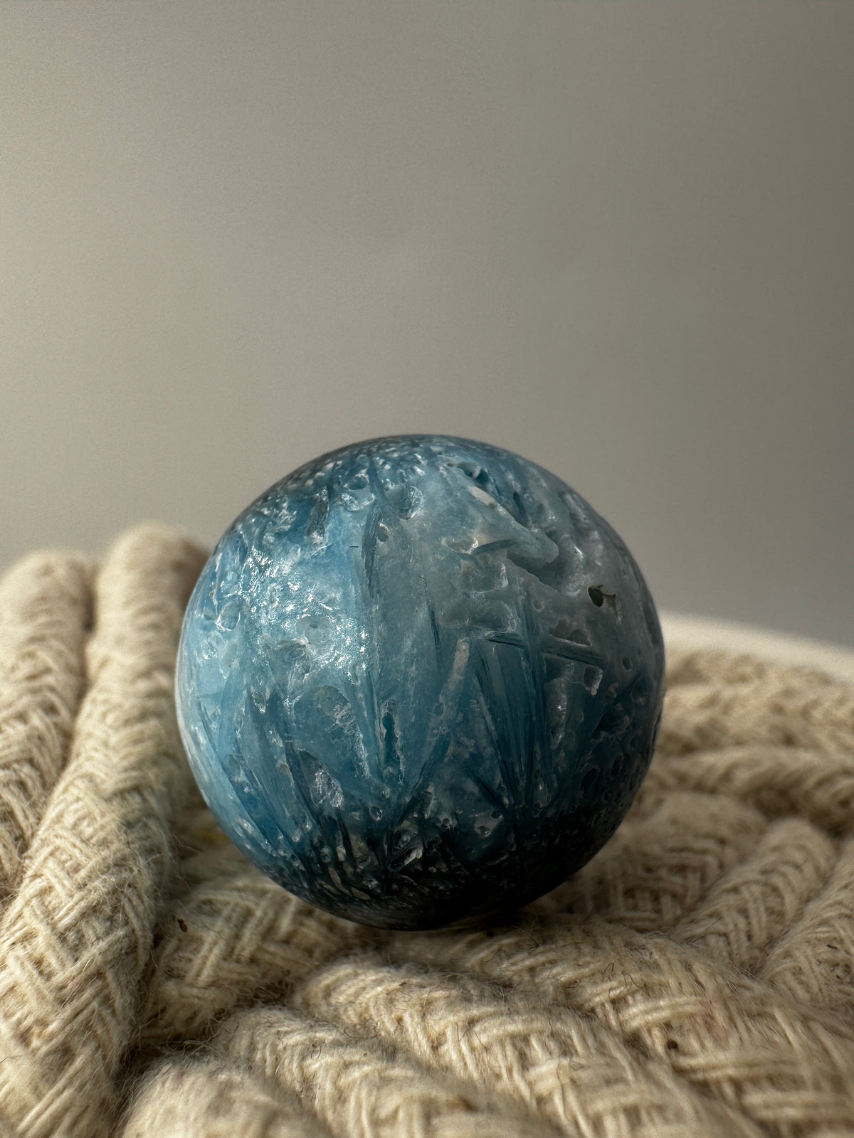 Eine perfekt sphärische Kugel aus Blue Ice Glacierite, deren glänzende Oberfläche das Licht reflektiert und den Blick auf die einmalige Struktur freigibt.