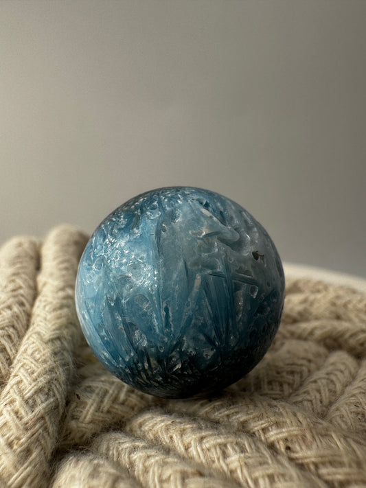 Eine perfekt sphärische Kugel aus Blue Ice Glacierite, deren glänzende Oberfläche das Licht reflektiert und den Blick auf die einmalige Struktur freigibt.