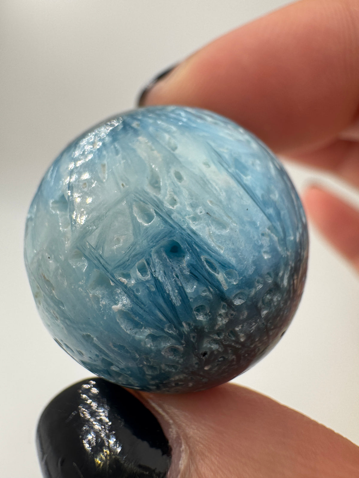 Eine perfekt sphärische Kugel aus Blue Ice Glacierite, deren glänzende Oberfläche das Licht reflektiert und den Blick auf die einmalige Struktur freigibt.