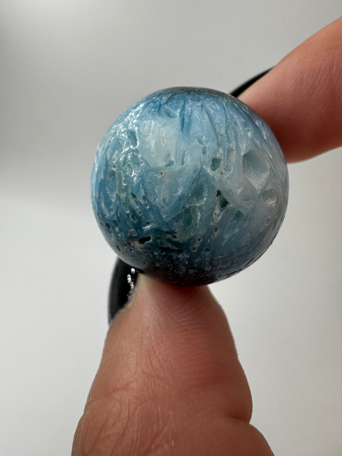 Eine perfekt sphärische Kugel aus Blue Ice Glacierite, deren glänzende Oberfläche das Licht reflektiert und den Blick auf die einmalige Struktur freigibt.