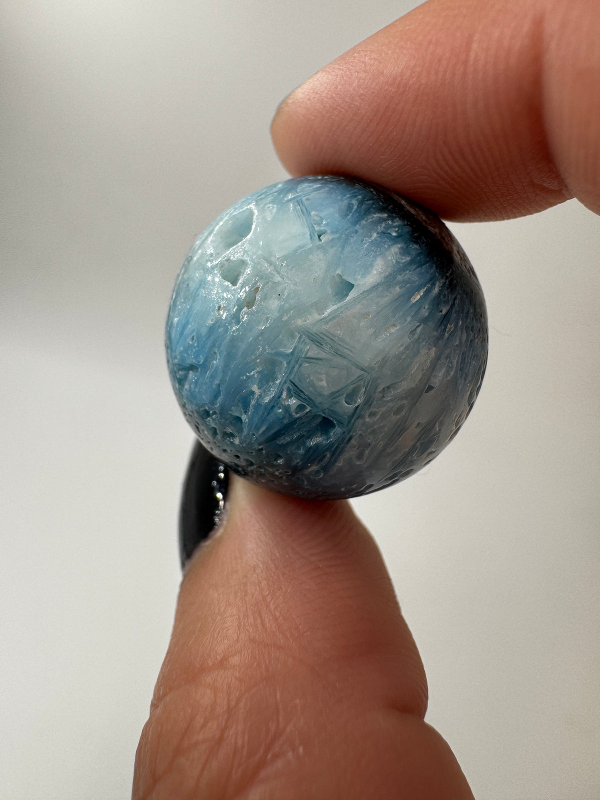 Eine perfekt sphärische Kugel aus Blue Ice Glacierite, deren glänzende Oberfläche das Licht reflektiert und den Blick auf die einmalige Struktur freigibt.