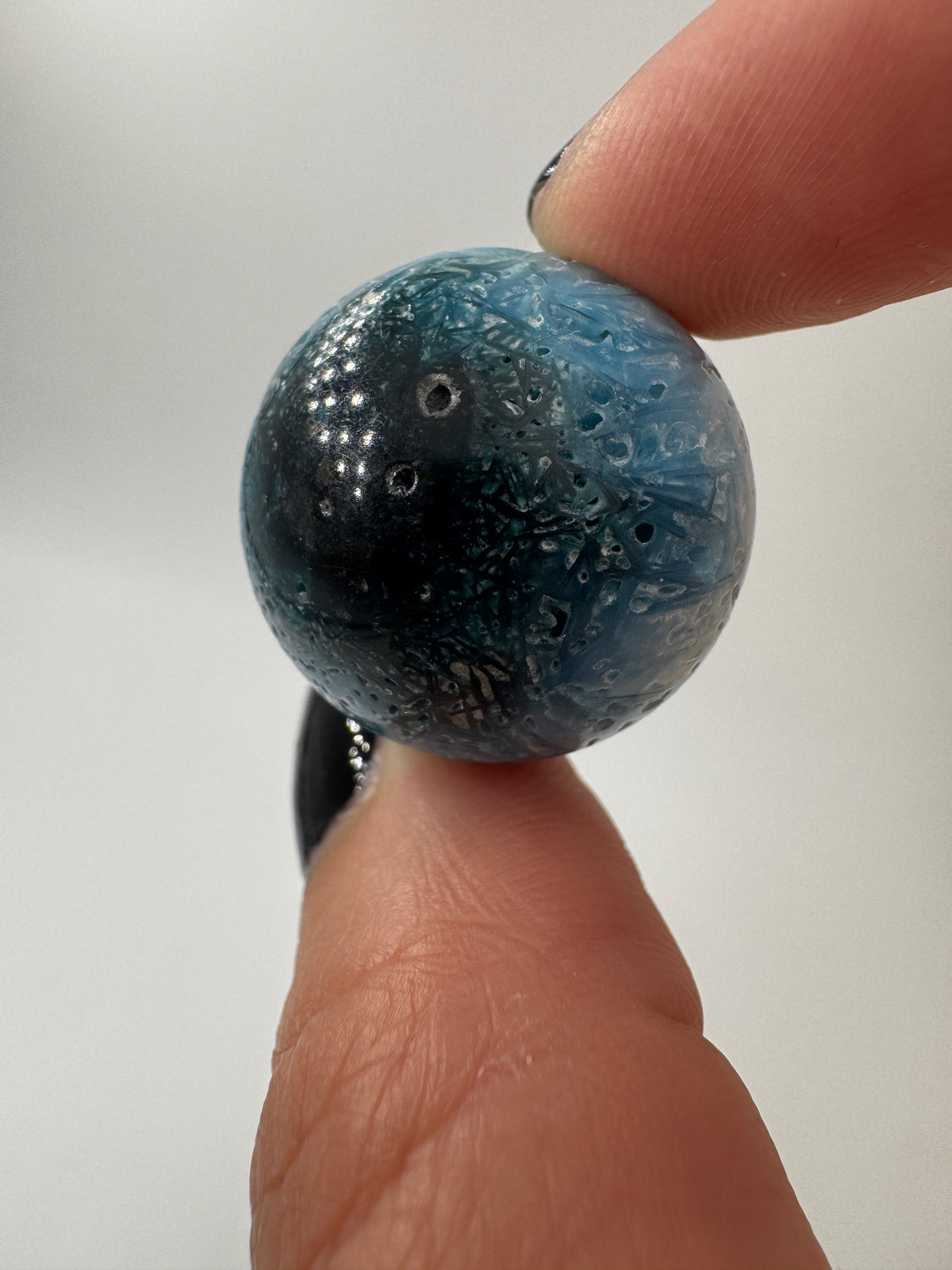 Eine perfekt sphärische Kugel aus Blue Ice Glacierite, deren glänzende Oberfläche das Licht reflektiert und den Blick auf die einmalige Struktur freigibt.