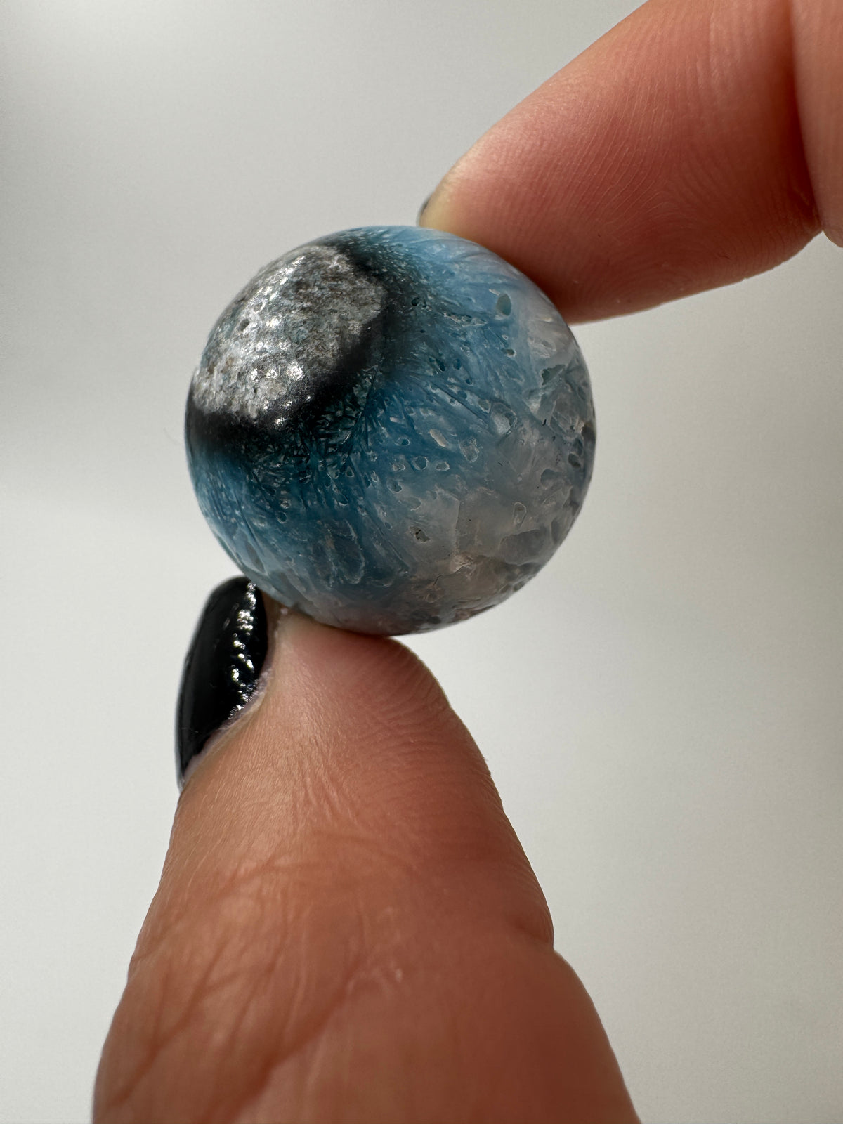 Eine perfekt sphärische Kugel aus Blue Ice Glacierite, deren glänzende Oberfläche das Licht reflektiert und den Blick auf die einmalige Struktur freigibt.