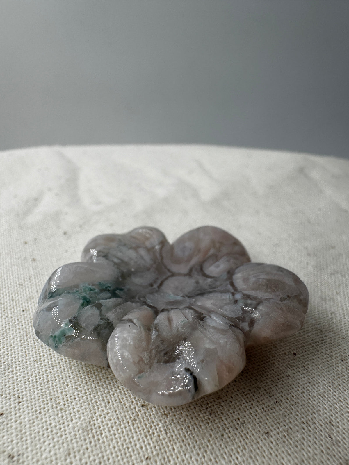 Eine detailreiche Skulptur in Blumenform aus zartrosa Blumenachat mit deutlich erkennbaren, weißen sphärolithischen Einschlüssen.