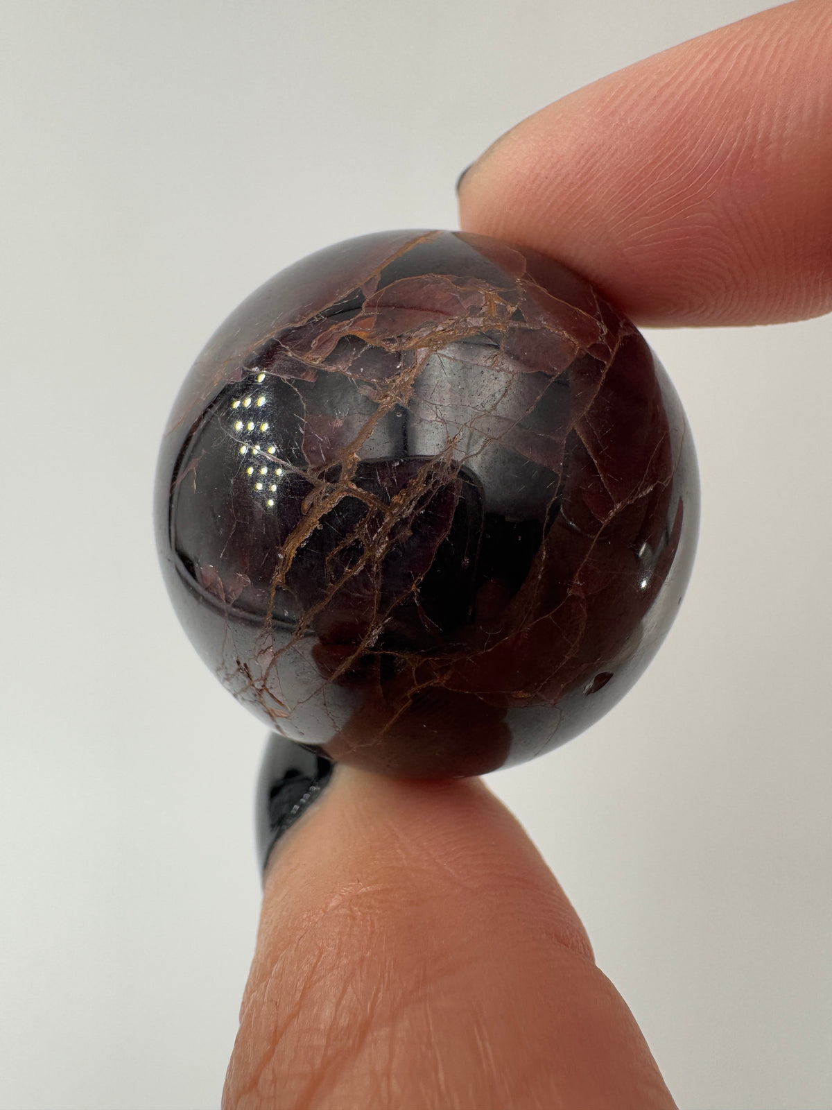 Eine polierte Kugel aus tiefrotem Granat  zeigt unter punktuellem Licht seidige Reflexionen sowie die typische mineralische Textur.