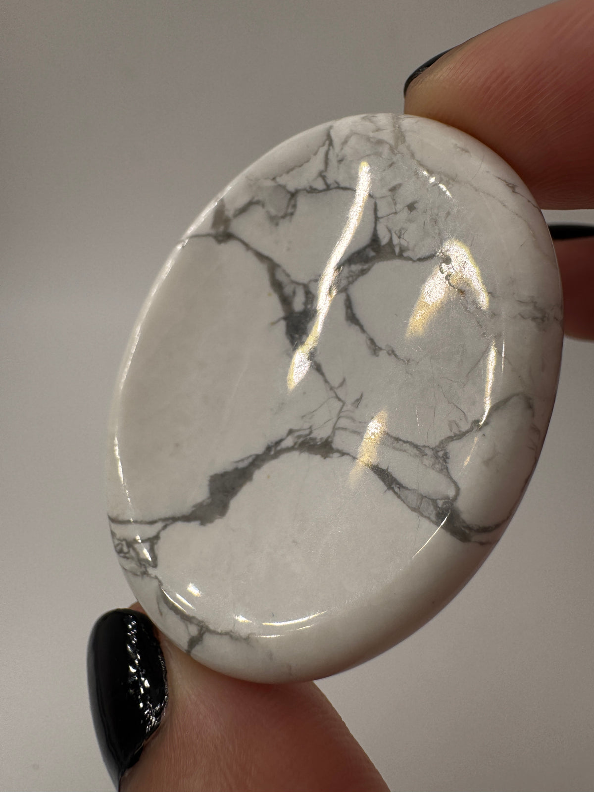 Ein  Daumensteinen aus Howlit mit glänzend polierten Oberflächen und zentraler Daumenmulde.