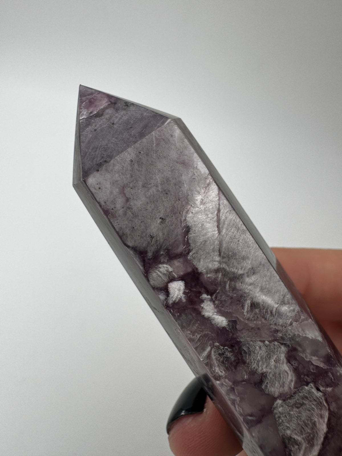 Ein spitz zulaufender, polierter Turm aus fliederfarbenem Lepidolith mit dezent glitzernden Glimmer-Einschlüssen