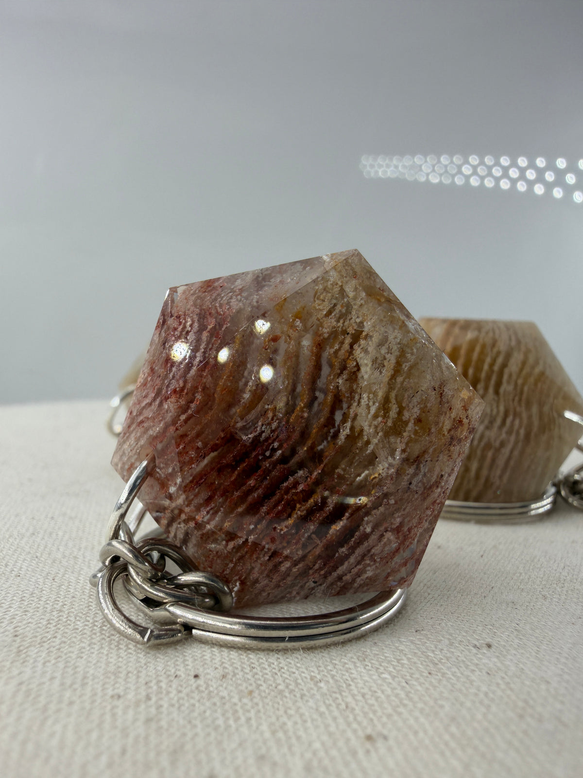 Ein klarer Lodolith-Anhänger in sechseckiger Form mit dichten, schichtartigen Einschlüssen in Erdtönen an einem stabilen Metallring.