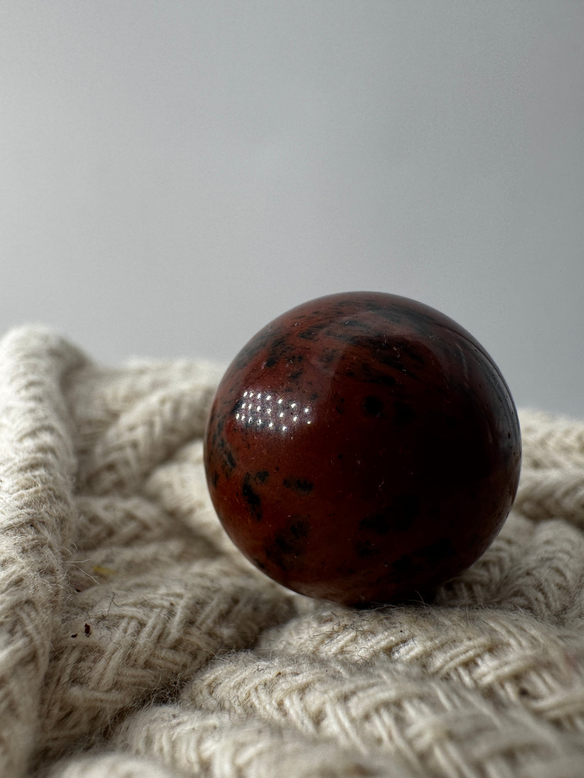 Mehrere hochglanzpolierte Mahagoni-Obsidian Minikugeln mit einer markanten rot-schwarzen Fließtextur, arrangiert auf einer hellen Unterlage.