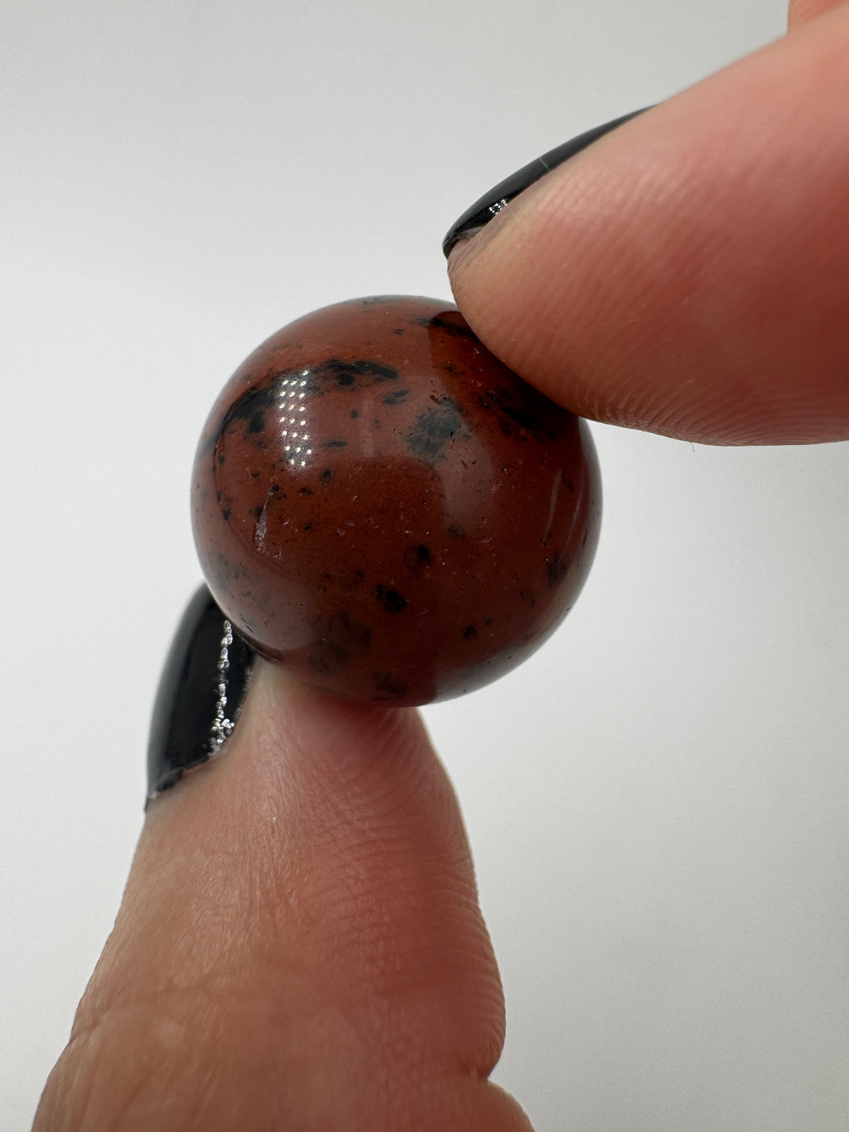 Eine Mahagoni-Obsidian Minikugel mit einer markanten rot-schwarzen Fließtextur.
