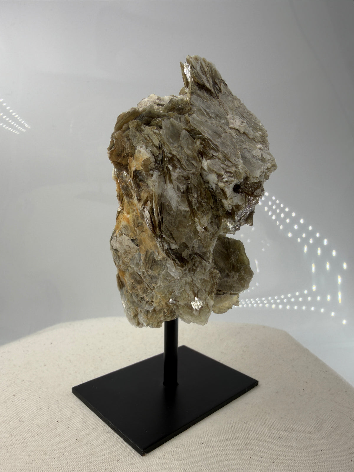 Silbrig glänzender Muskovit-Glimmer auf einem schwarzen Metallständer zur dekorativen Präsentation.