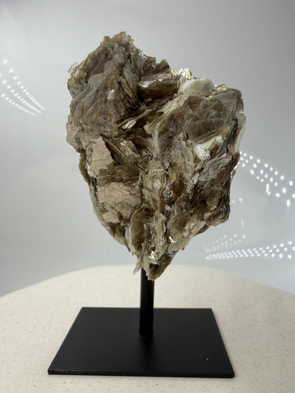 Silbrig glänzender Muskovit-Glimmer auf einem schwarzen Metallständer zur dekorativen Präsentation.