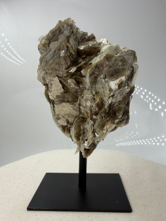 Silbrig glänzender Muskovit-Glimmer auf einem schwarzen Metallständer zur dekorativen Präsentation.