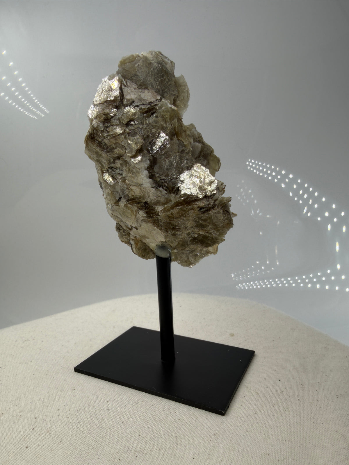 Silbrig glänzender Muskovit-Glimmer auf einem schwarzen Metallständer zur dekorativen Präsentation.