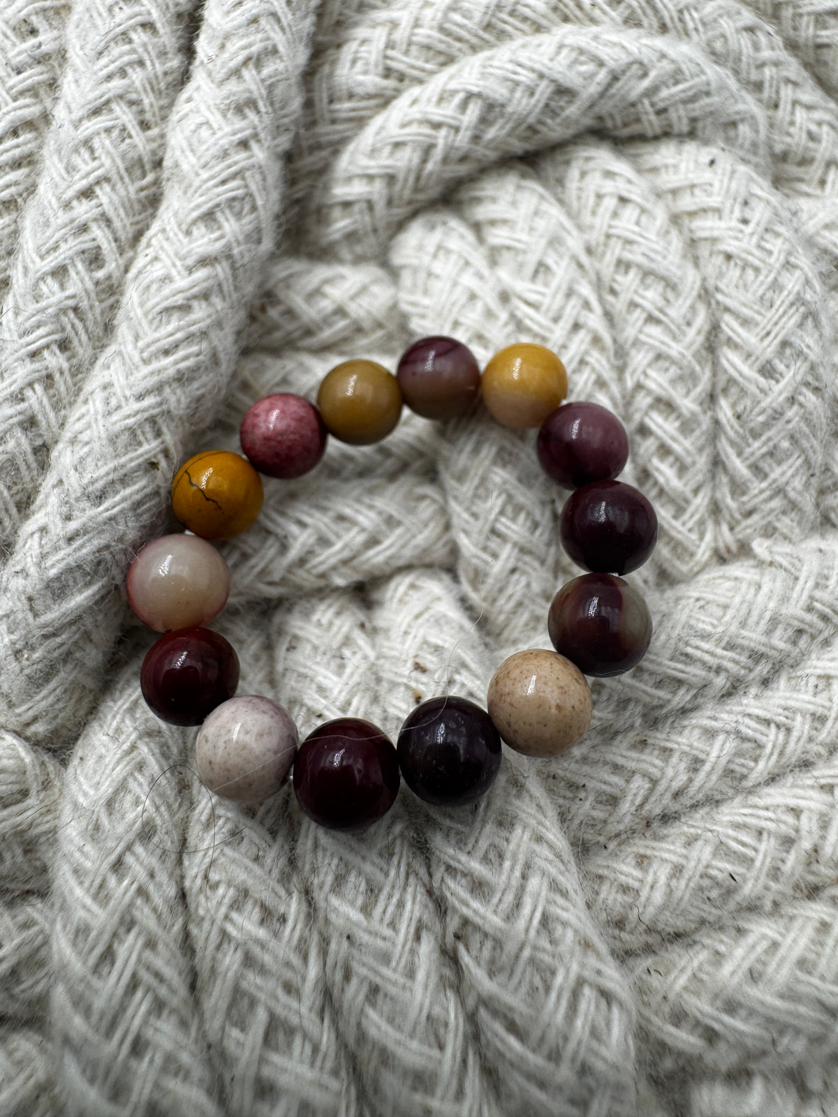 Elastischer Ring aus Mookait mit 4,6-mm-Kugeln – warme Erdtöne in Ocker, Bordeaux und Creme, Ringdurchmesser 5,5–6 cm.