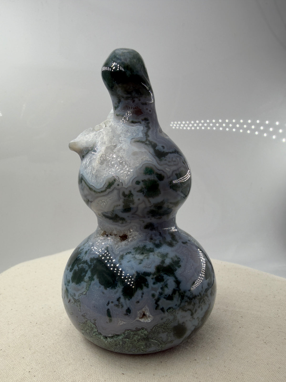 Eine polierte Skulptur in Form eines Flaschenkürbisses aus Moosachat mit tiefgrünen, moosartigen Strukturen in einer milchig-transparenten Matrix.