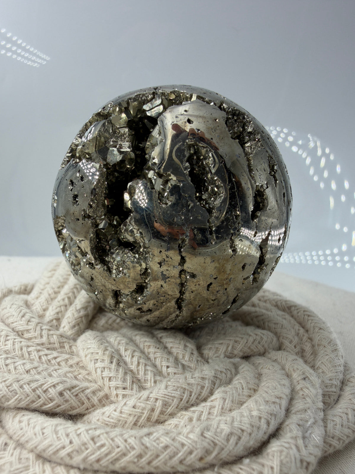 Eine hochglänzende, metallisch Pyrit-Kugel, deren spiegelnde Oberfläche die Umgebung reflektiert und winzige, natürliche Kristallstrukturen offenbart.