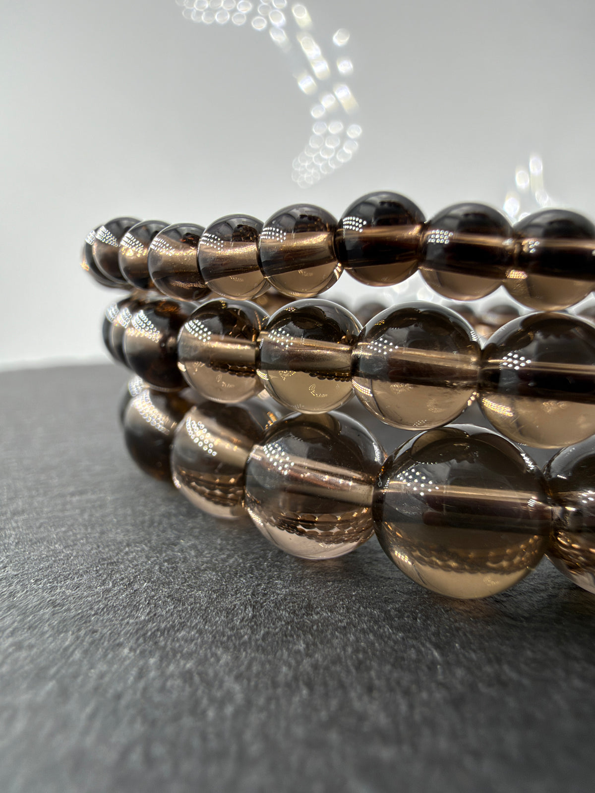Rauchquarz-Armbänder mit glänzenden, durchscheinenden braunen Kugelperlen in drei Größen auf dunklem Untergrund.