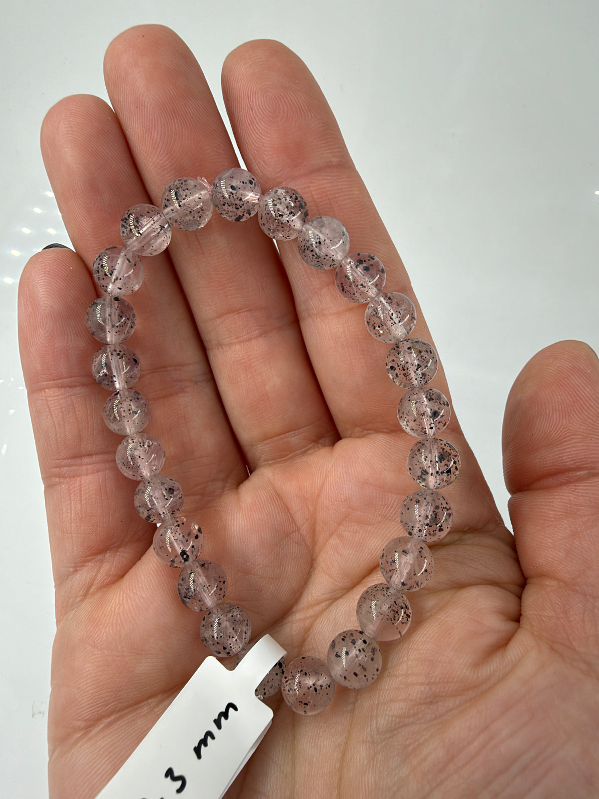 Rosenquarz-Hämatit-Armband RM22 mit zartrosa Kugelperlen und dunklen Einschlüssen auf einer offenen Hand.