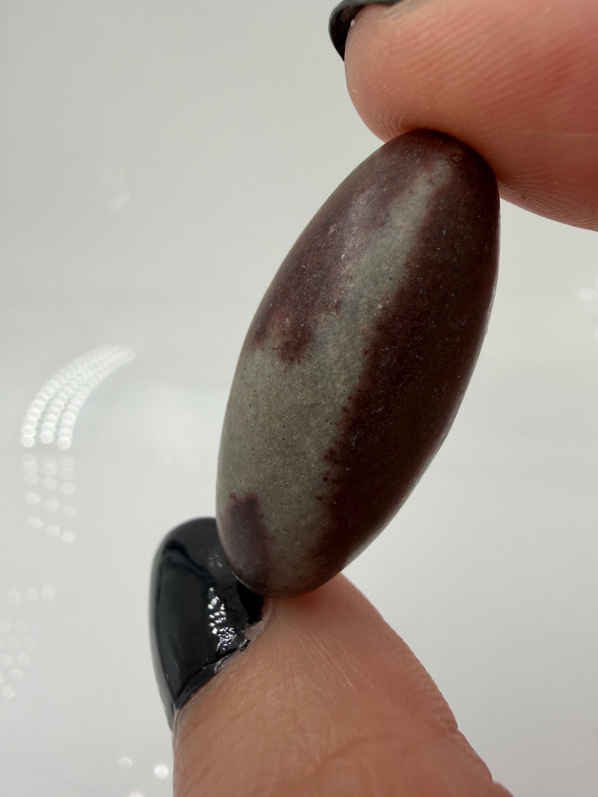 Kleiner, elliptisch geformter Shiva Lingam aus Indien mit markanter braun-roter Bänderung und glatter Oberfläche.