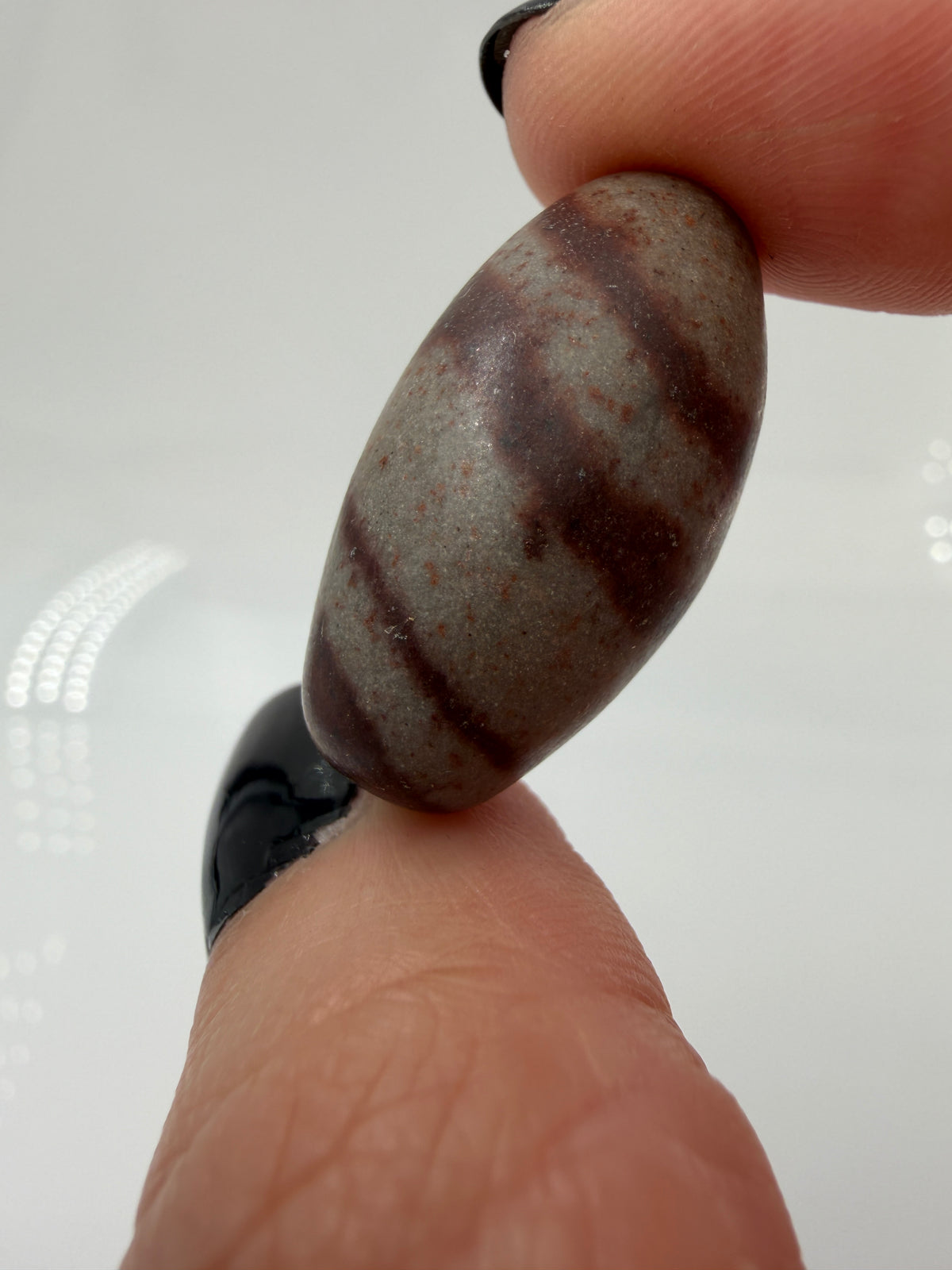 Kleiner, elliptisch geformter Shiva Lingam aus Indien mit markanter braun-roter Bänderung und glatter Oberfläche.