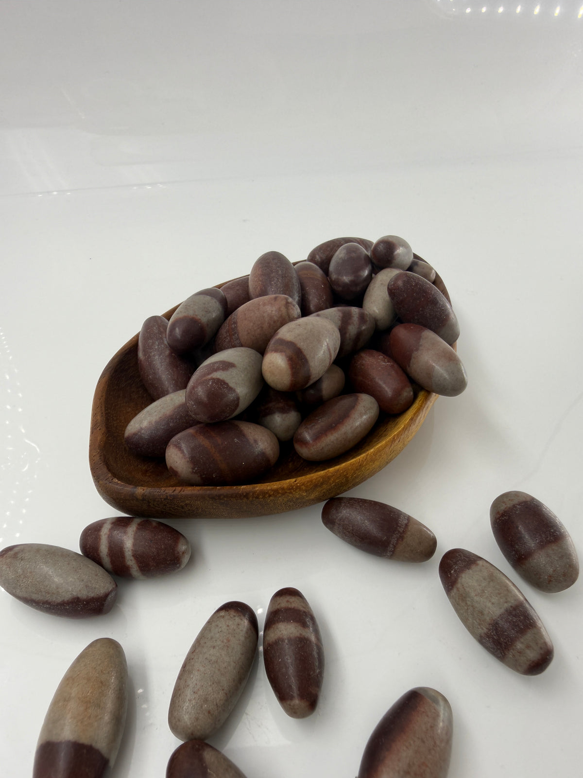 Kleiner, elliptisch geformter Shiva Lingam aus Indien mit markanter braun-roter Bänderung und glatter Oberfläche.