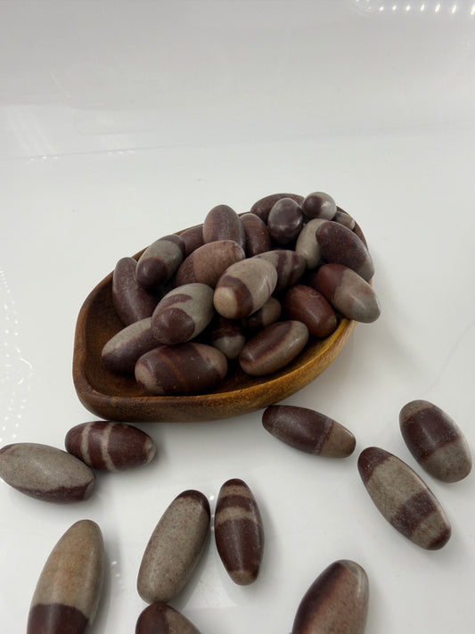 Kleiner, elliptisch geformter Shiva Lingam aus Indien mit markanter braun-roter Bänderung und glatter Oberfläche.