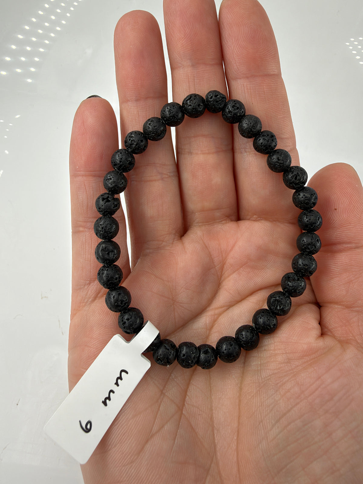 Vulkangestein-Armband LG6 mit schwarzen 6-mm-Kugelperlen auf einer offenen Hand.