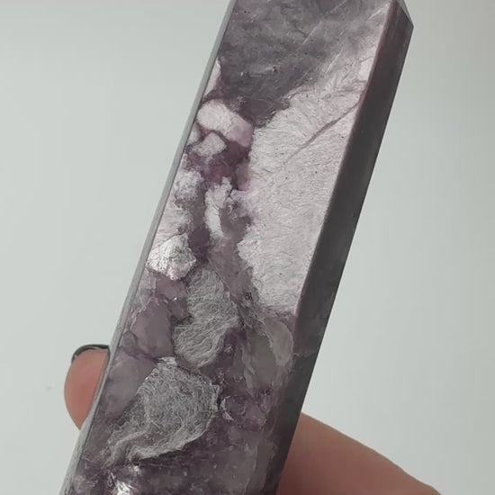 Ein spitz zulaufender, polierter Turm aus fliederfarbenem Lepidolith mit dezent glitzernden Glimmer-Einschlüssen
