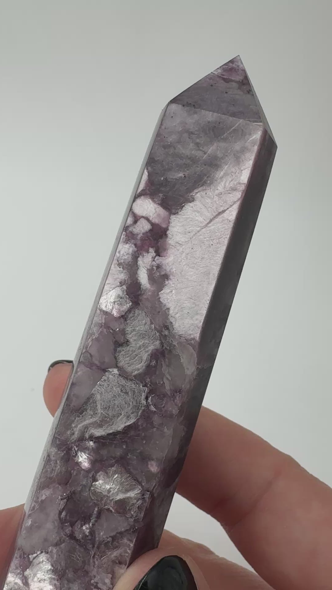 Ein spitz zulaufender, polierter Turm aus fliederfarbenem Lepidolith mit dezent glitzernden Glimmer-Einschlüssen